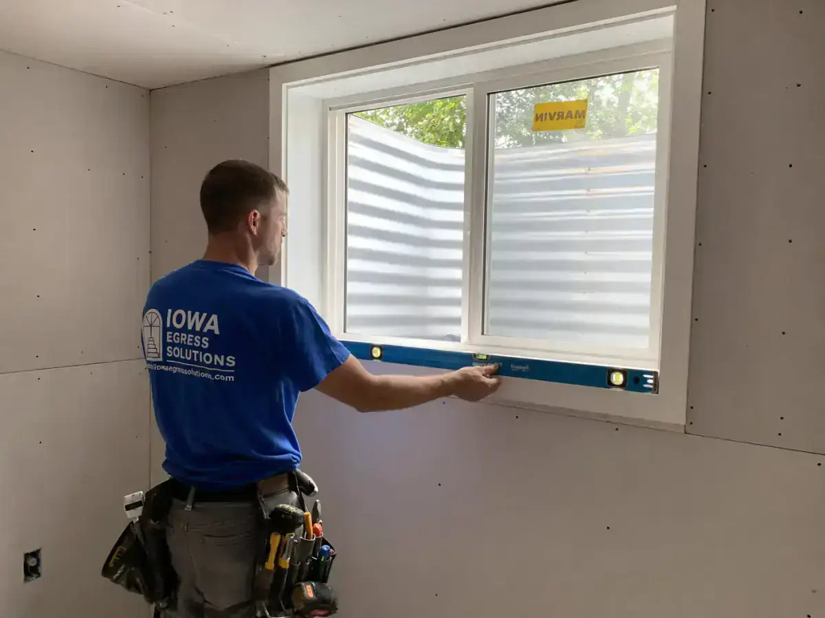 Egress window installers finishing interior cut and trim around a basement escape opening in Iowa